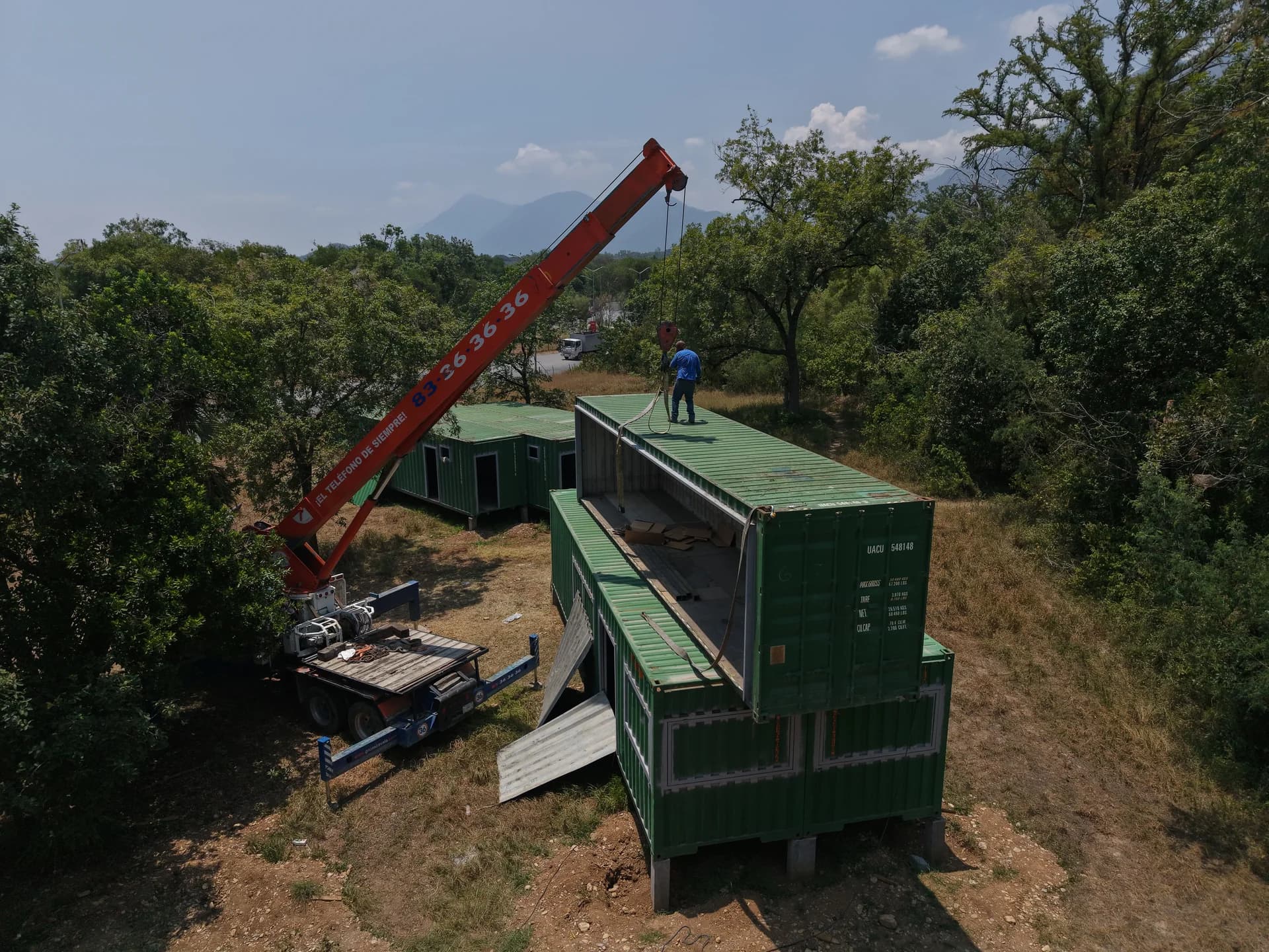 Grúa colocando módulo contenedor en segunda planta con montañas de Monterrey al fondo